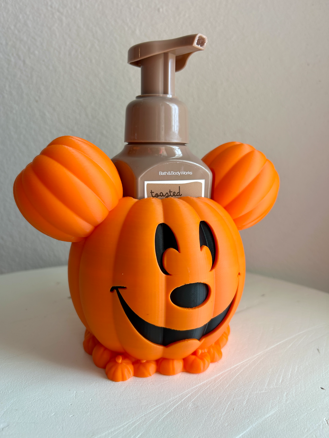 Halloween Pumpkin Soap Dispenser Holder in Orange — front view with pump soap bottle inside showing grinning jack-o'-lantern face and pumpkin ears