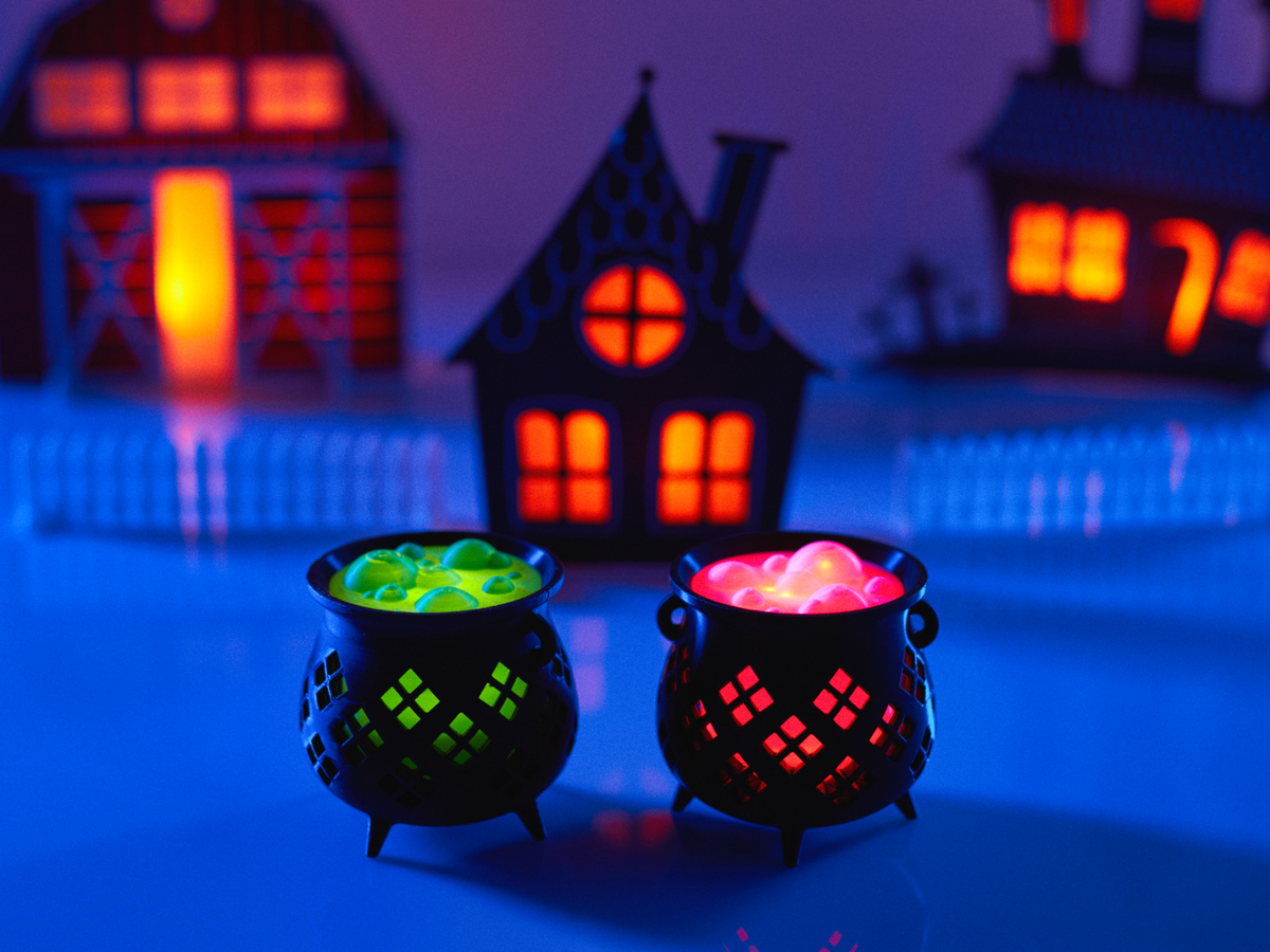 Halloween Cauldron Tealight Holder — two cauldrons side by side showing green and pink glowing tops with diamond lattice glow effect against haunted house backdrop