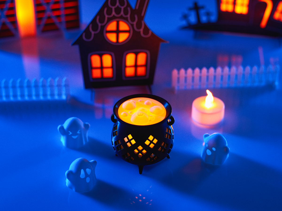Halloween Cauldron Tealight Holder — black cauldron with amber yellow glowing top casting diamond lattice light pattern with ghost figurines and tealight candle in Halloween scene