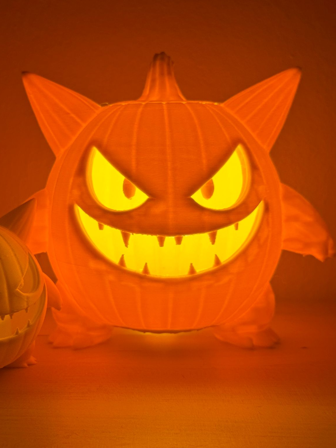 Monster Pumpkin Tealight Holder in Orange — front view showing fierce carved fanged face, pointed ears and clawed feet on wood surface