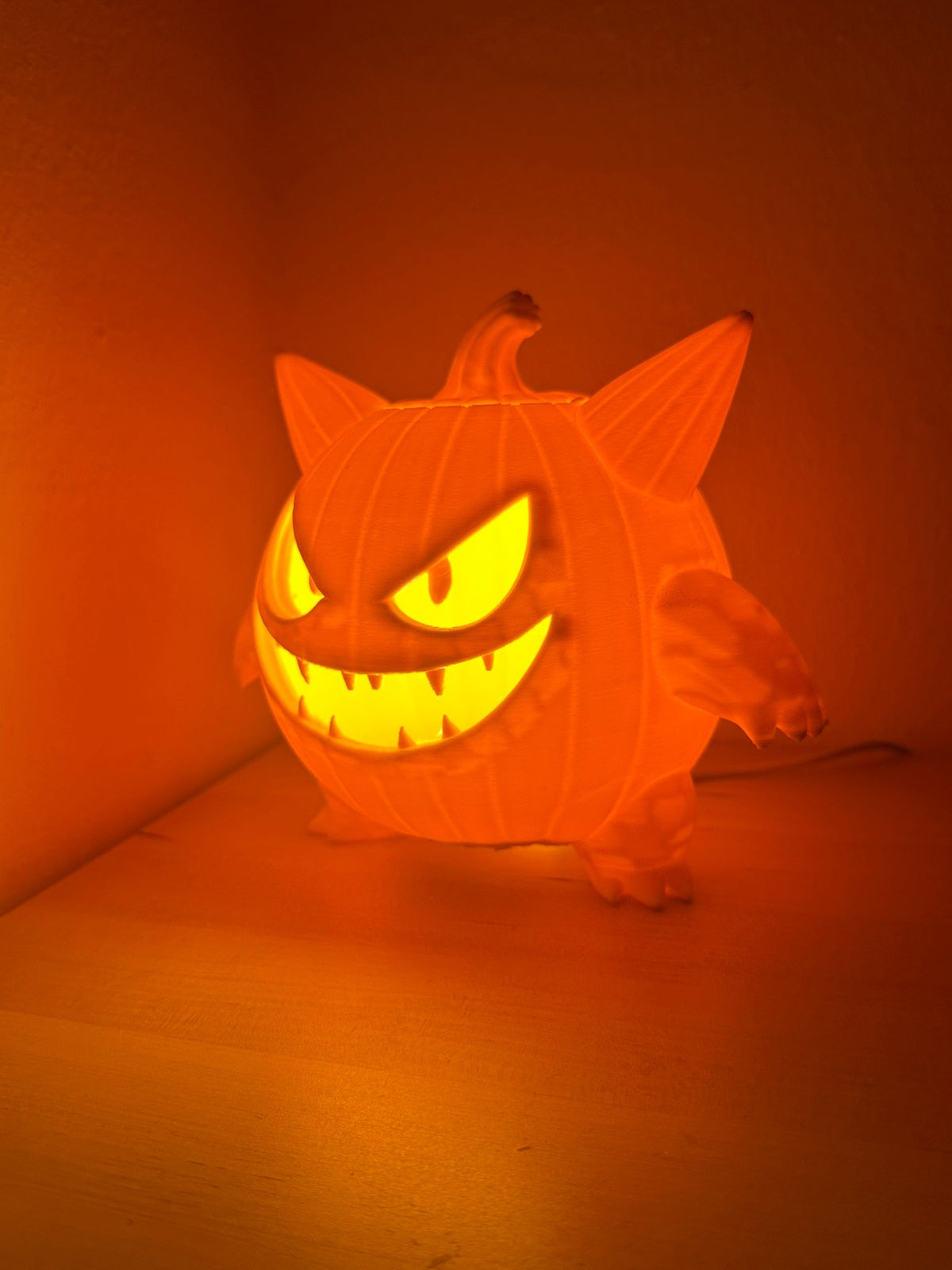 Monster Pumpkin Tealight Holder — rear three-quarter glow shot showing amber light through carved face from side angle against orange background