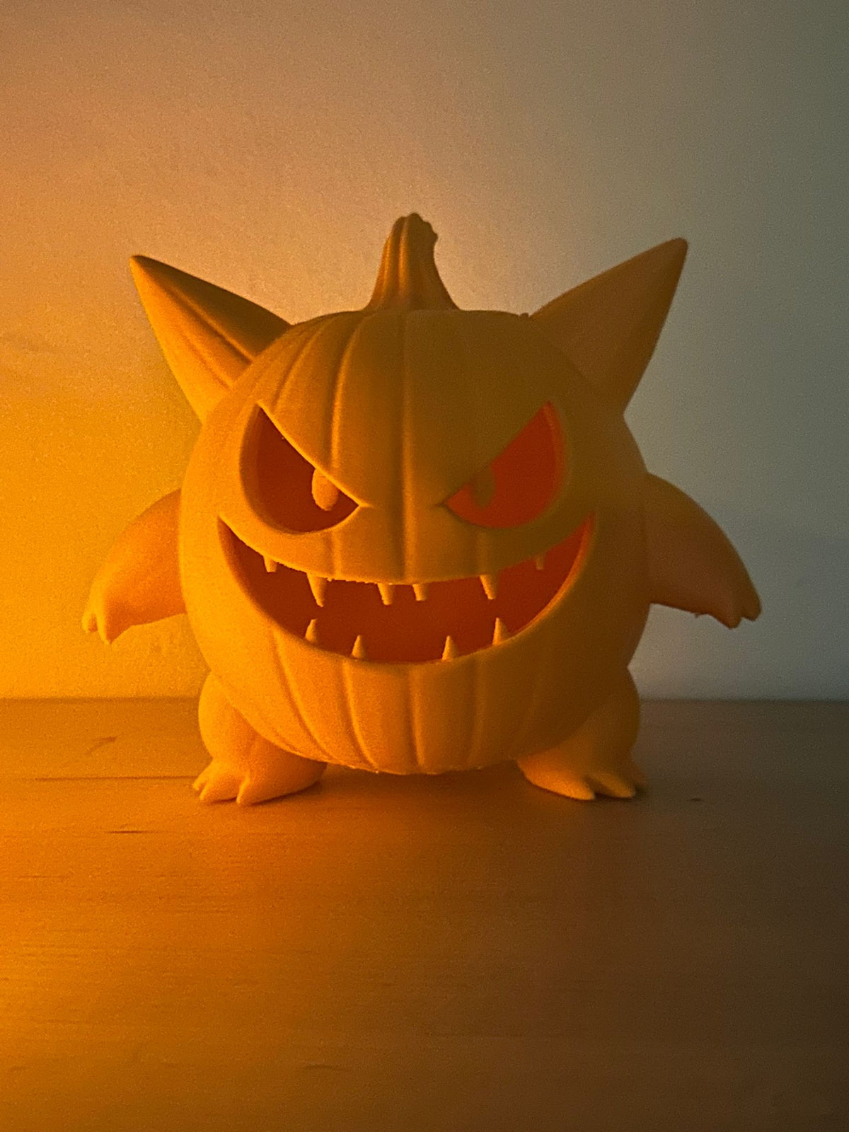 Monster Pumpkin Tealight Holder — close-up front glow shot showing amber light blazing through carved eyes and fanged mouth against orange background