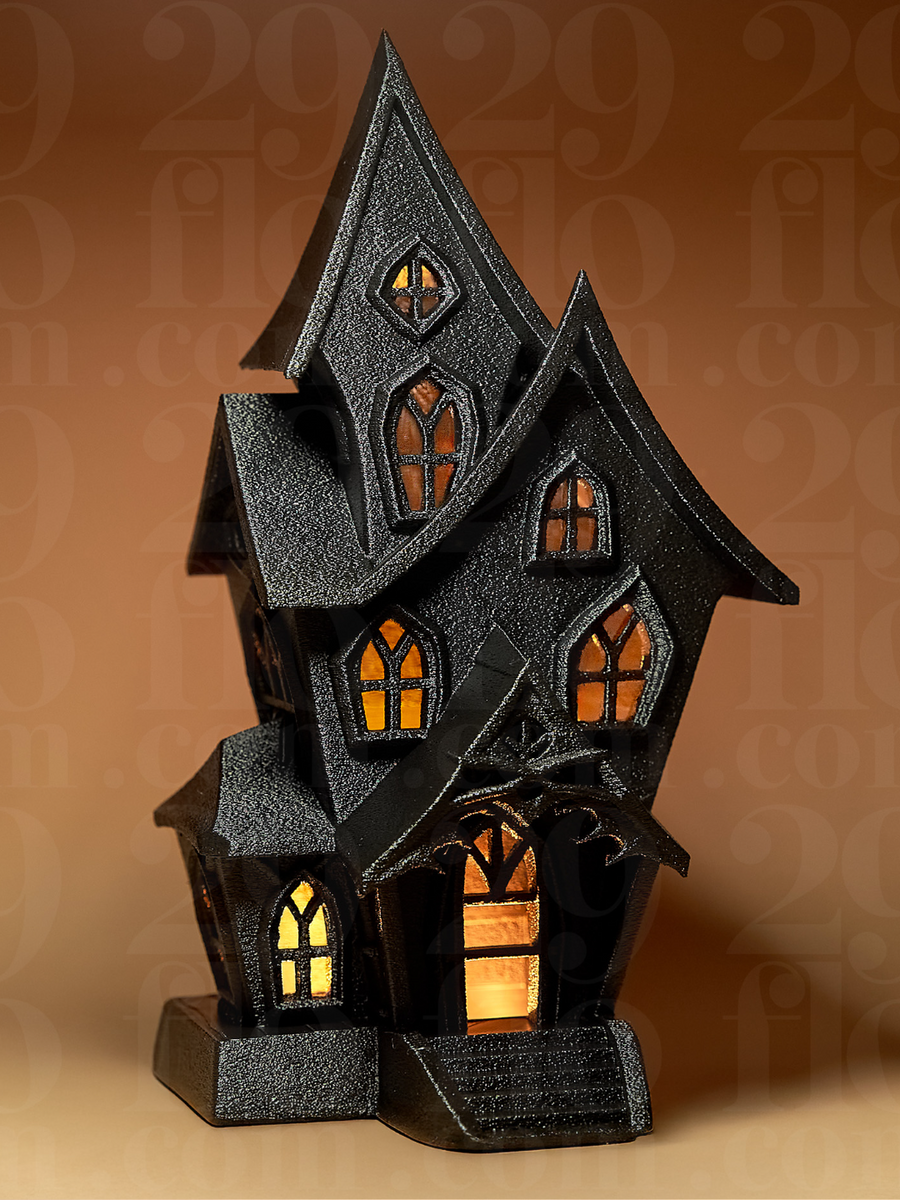 Haunted House Tealight Holder in Black — front view glowing amber through gothic arched windows and open doorway with dead tree detail