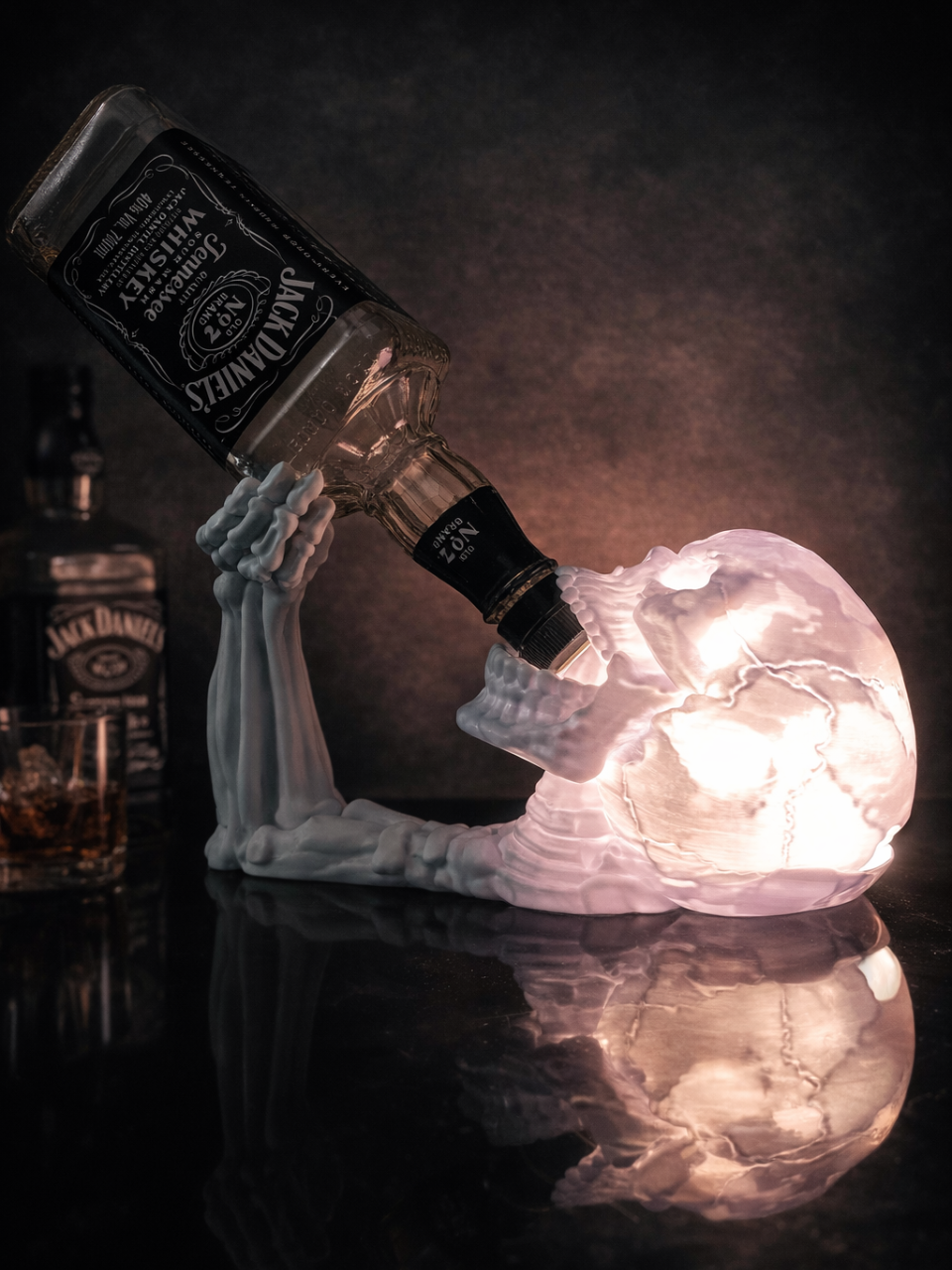 Skeleton Arm and Skull Bottle Holder in illuminated clear — skull and arm glowing with internal LED light holding a bottle at reclining angle on dark reflective surface
