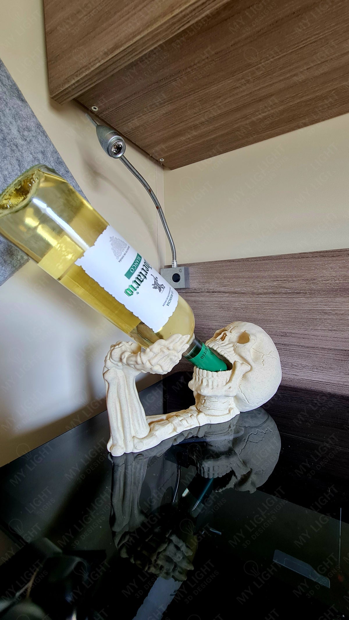 Skeleton Arm and Skull Bottle Holder in bone white — side view holding wine bottle showing full reclining skeleton upper body sculpt on glass surface