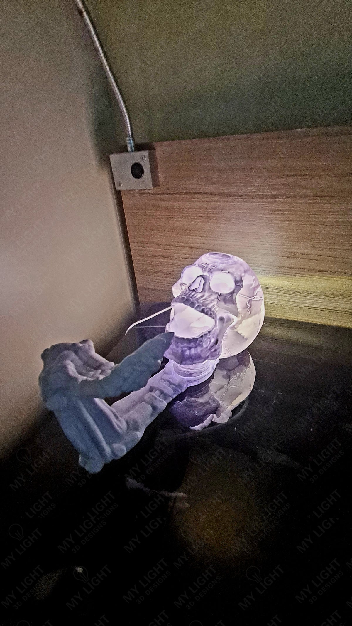 Skeleton Arm and Skull Bottle Holder in illuminated clear — rear three-quarter view glowing purple-blue with LED illumination on dark glass surface