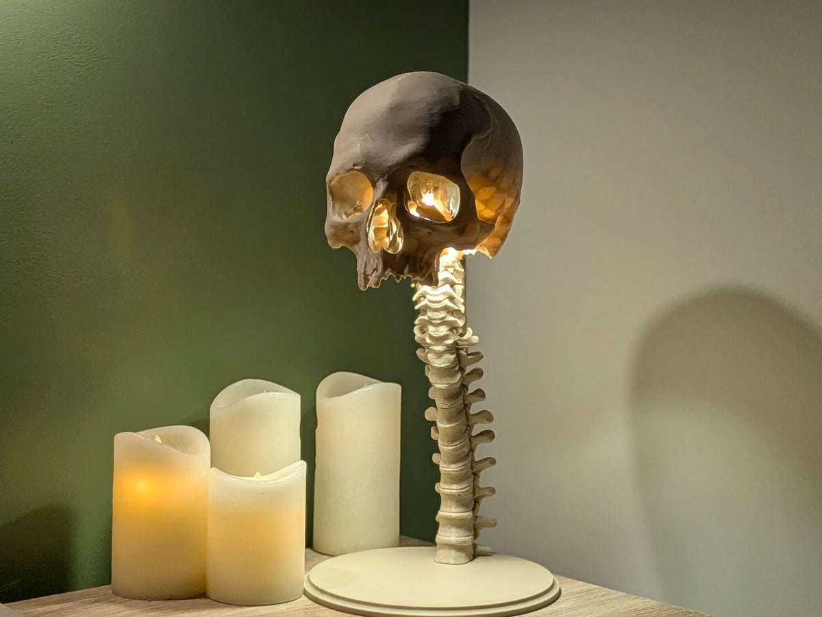Skull and Spine Tealight Lamp — side three-quarter view showing full spine column detail, skull tilt and amber glow with LED candles beside it on wooden shelf