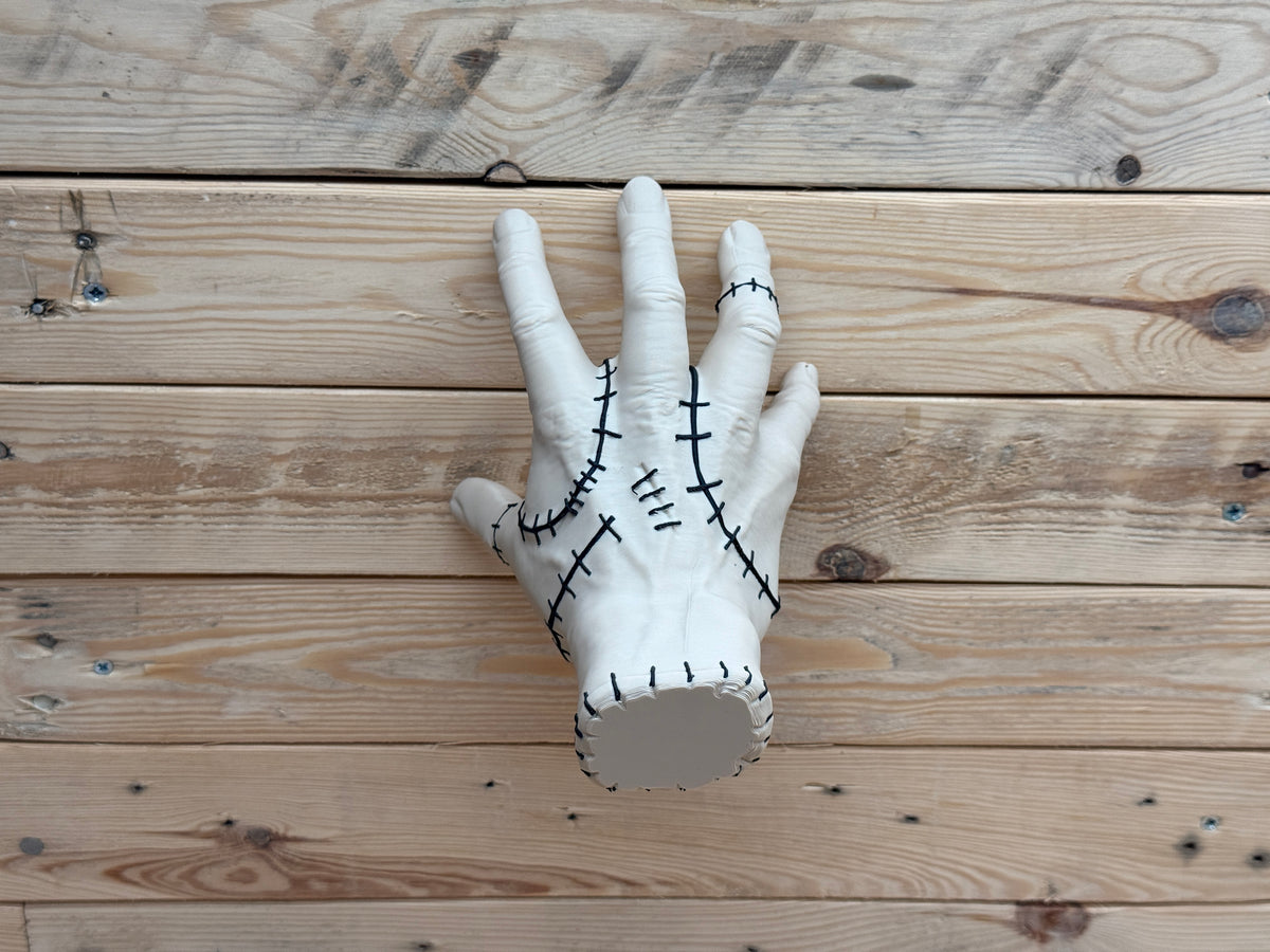 Thing Hand Model — palm-up view showing black cross-stitch detail across back of hand and finger joints on wood background