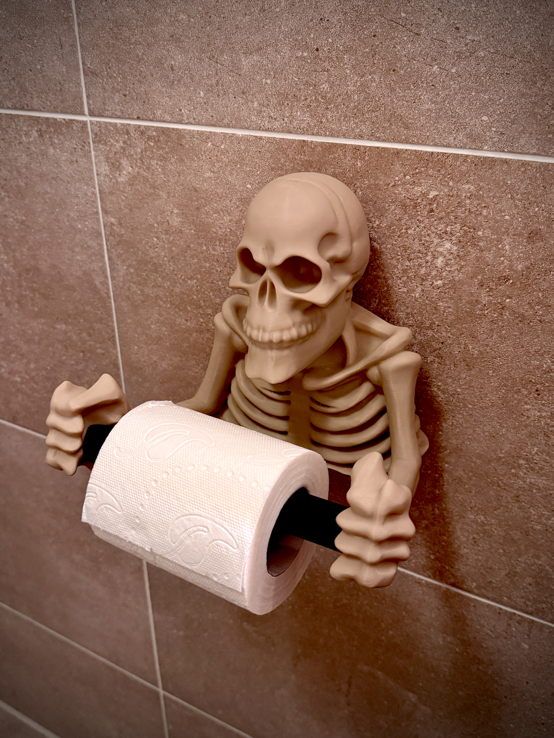 Skeleton toilet roll holder white bone colour full skeleton upper body emerging from wall holding black metal toilet roll bar with full toilet roll loaded full ribcage detail anatomical skull face wall mounted bathroom in use shot