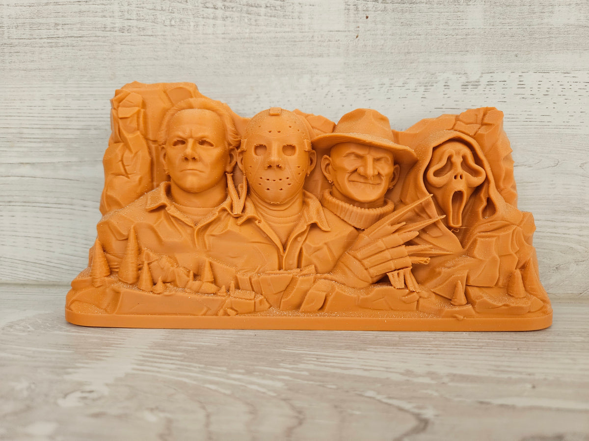 Mount Horrormore sculpture — front view showing four horror icon relief carvings in terracotta stone finish against light wood background