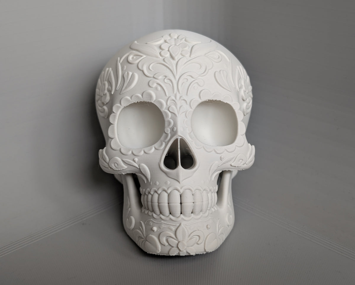 Day of the Dead Floral Skull Sculpture in white — front view showing full raised botanical floral relief across cranium, around orbital cavities and jaw on grey background
