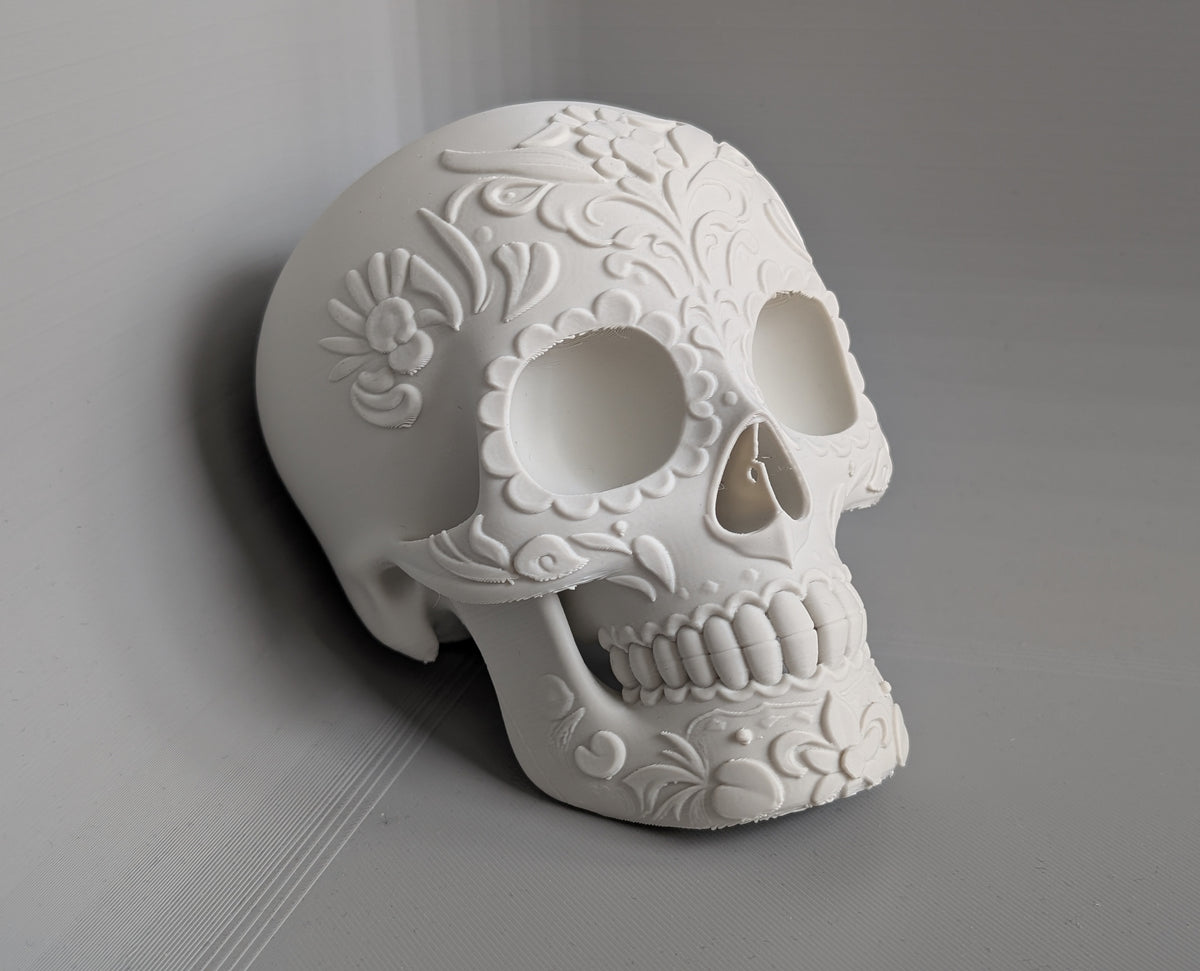 Day of the Dead Floral Skull Sculpture in white — three-quarter front view showing raised floral scrollwork across temporal region, orbital rim and cheekbone detail