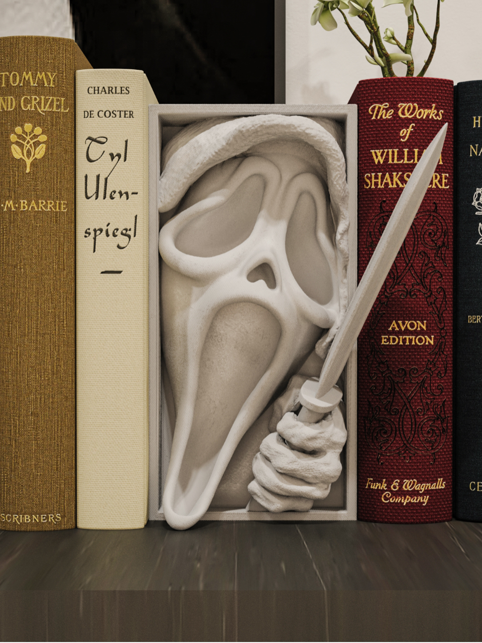 Scream book nook relief sculpture white rectangular framed box Ghostface mask flowing hooded robe screaming hollow mouth deep eye sockets clawed hand clutching knife blade displayed between vintage hardcover books on dark wooden bookshelf book nook styling front facing view