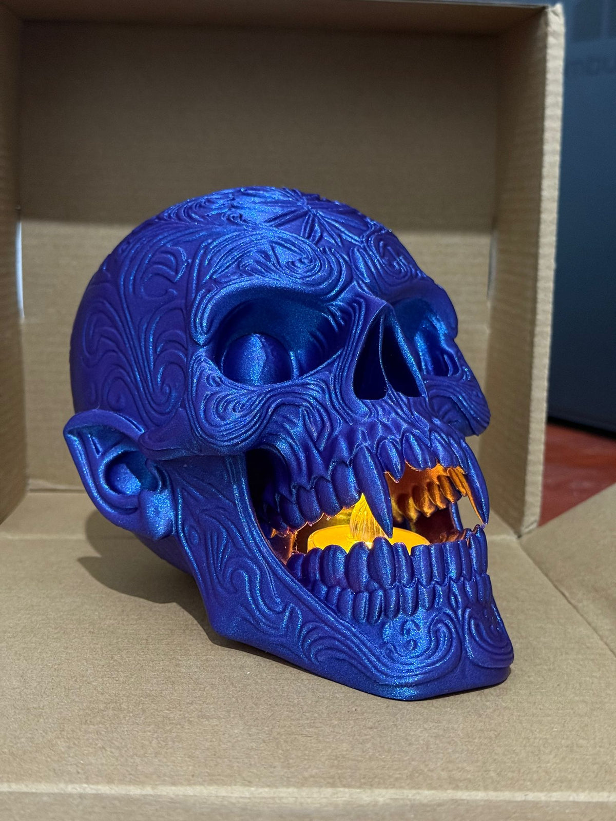 Skull Tealight Holder in blue metallic — side profile showing jaw open with amber tealight glow