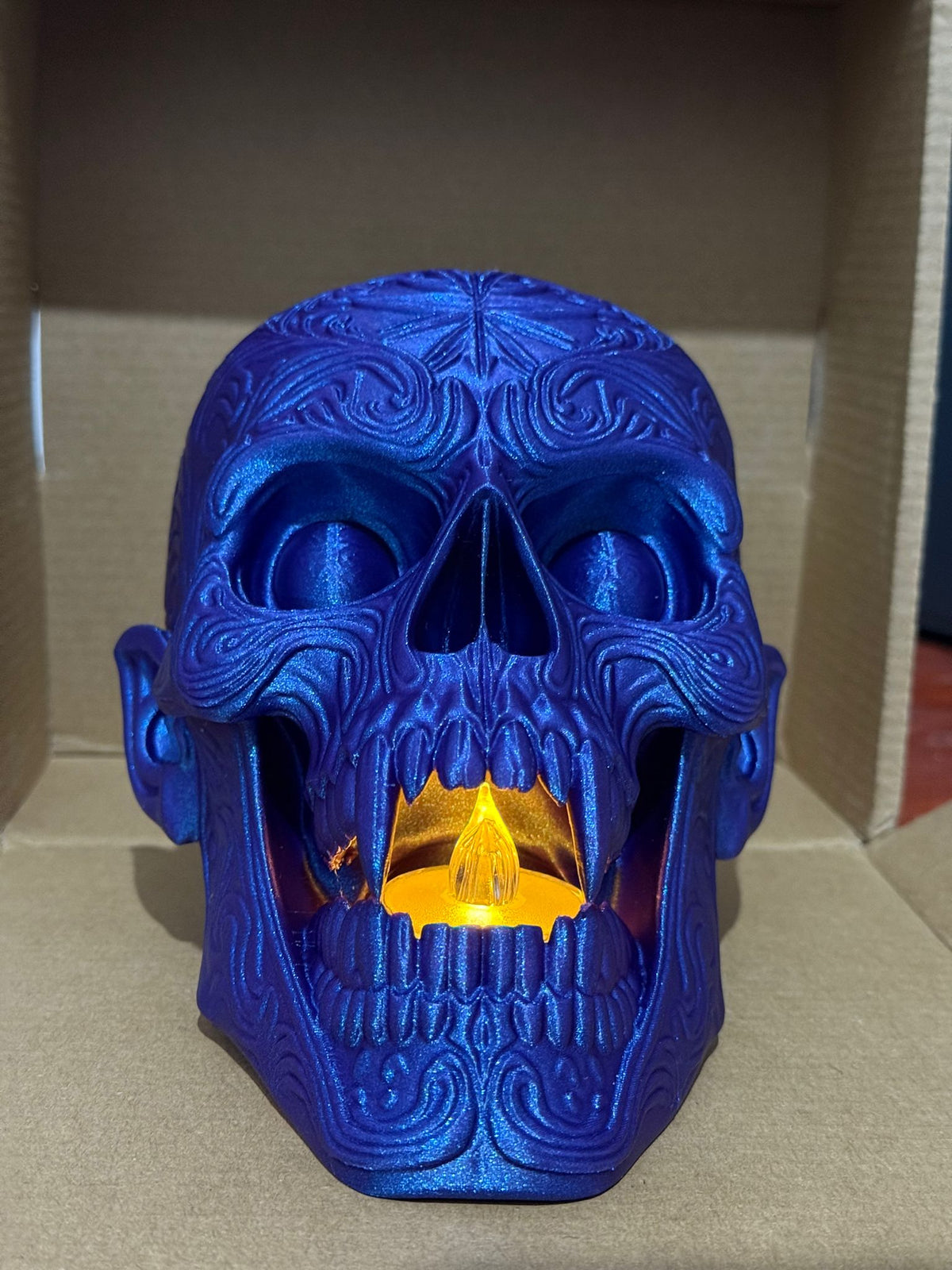Skull Tealight Holder in blue metallic — front face-on view with LED tealight glowing through teeth