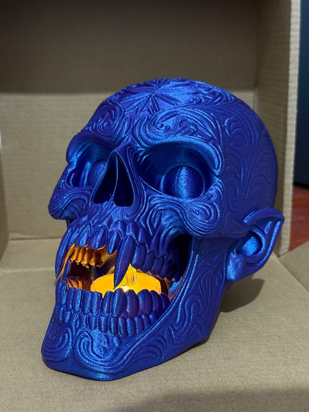 Skull Tealight Holder in blue metallic — angled side view showing full skull form and glowing fangs