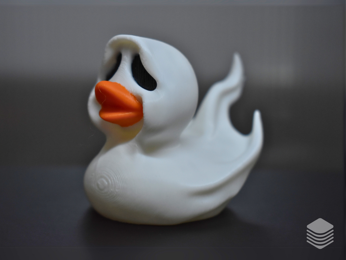 Halloween Ghost Duck Sculpture — right three-quarter view: white ghost sheet hood peak, two black teardrop void eyes and vivid orange bill visible from right angle, large flame-form ghost sheet drapes at rear right, matte white surface with natural drape fold lines