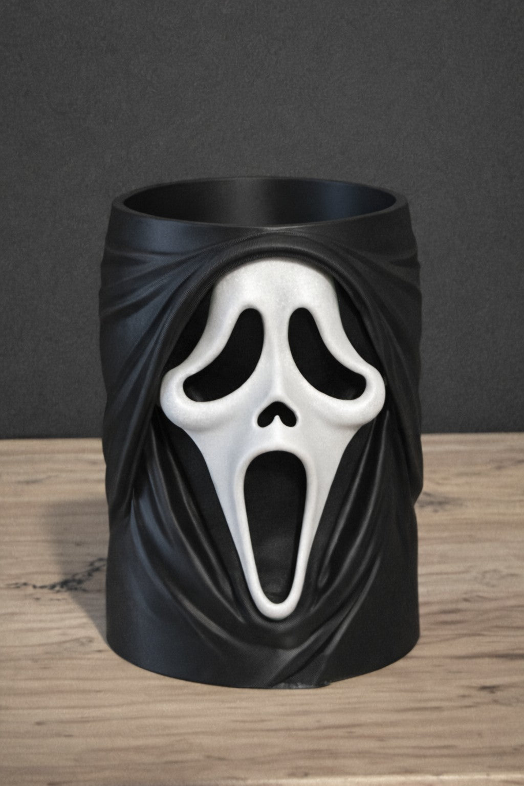 Ghostface Scream Can & Pen Holder — second front view showing elongated white Ghostface mask emerging from black draped robe folds, open cylindrical top on wooden surface