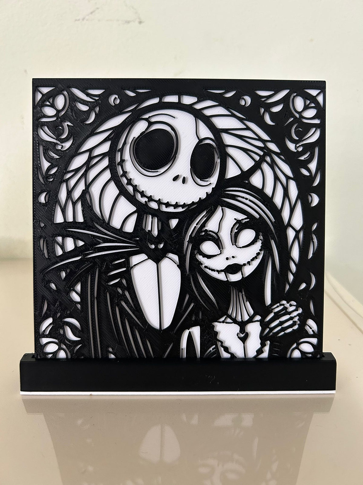 Jack & Sally Nightmare Before Christmas Shadow Box Display — slightly angled front view showing full composition clarity, Jack skull dome and Sally figure detail with swirling vine and rose border, white backplate visible through filigree apertures