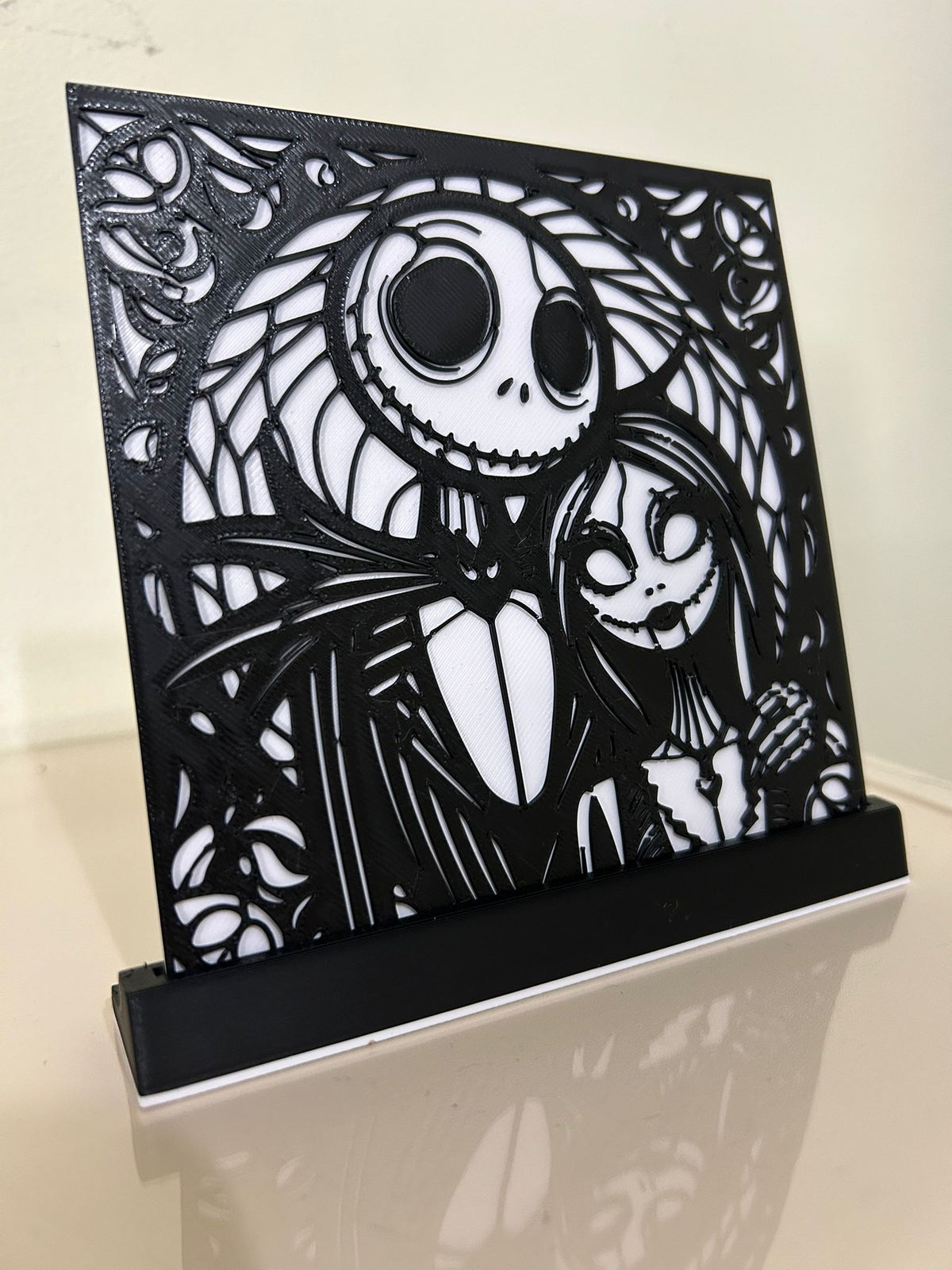 Jack & Sally Nightmare Before Christmas Shadow Box Display — three-quarter angle view showing two-layer shadow box depth, filigree overlay floating above white backplate in black rectangular desktop stand on reflective white surface