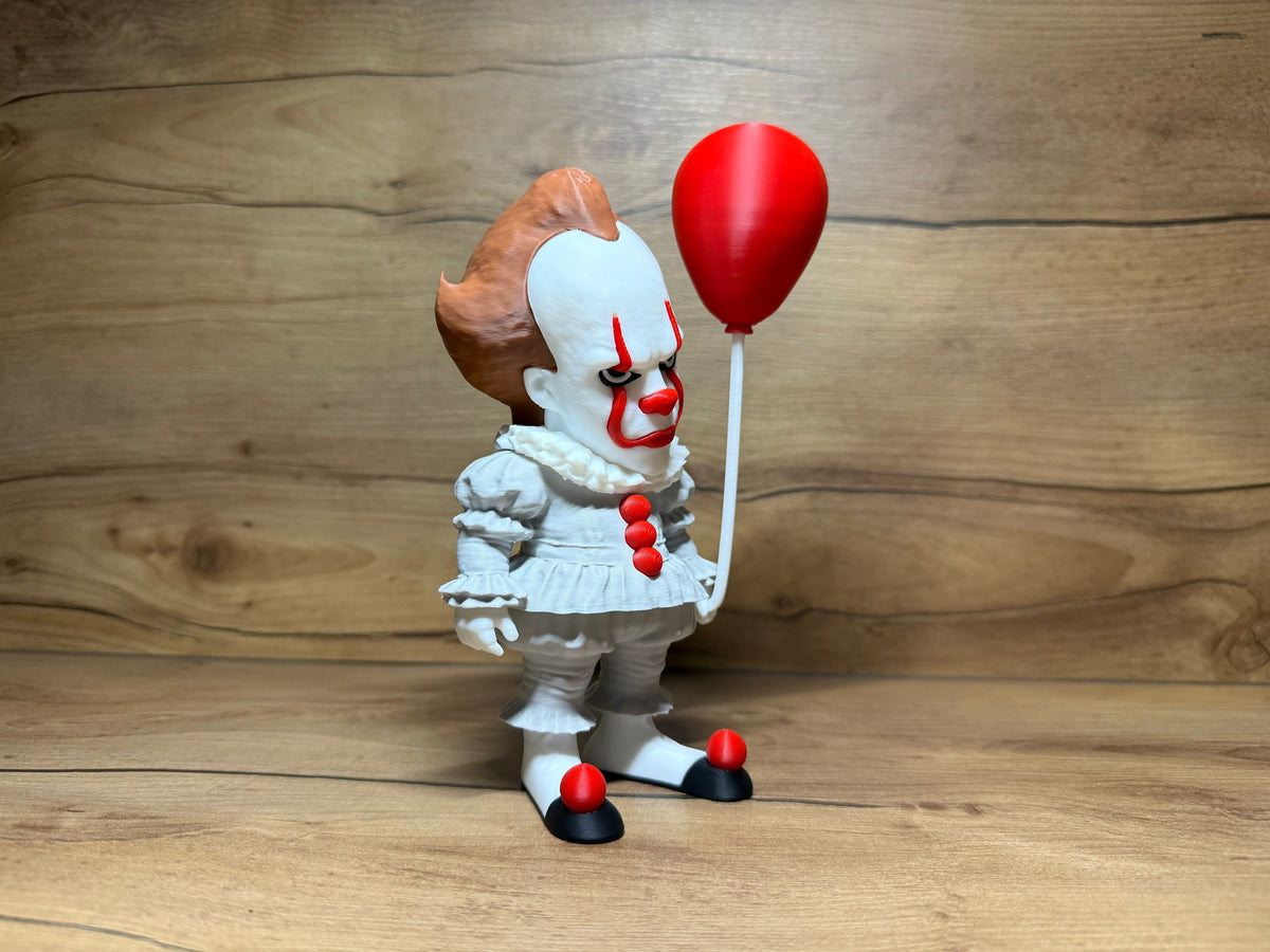 Pennywise IT Horror Minifigure Sculpture — right front three-quarter view showing full face character detail including red brow arch, yellow-gold eye, red nose, red smile lines, auburn hair tuft profile, white Elizabethan collar depth, three red pompom buttons on torso, right arm extended holding red balloon at head height and red pompom shoe toe