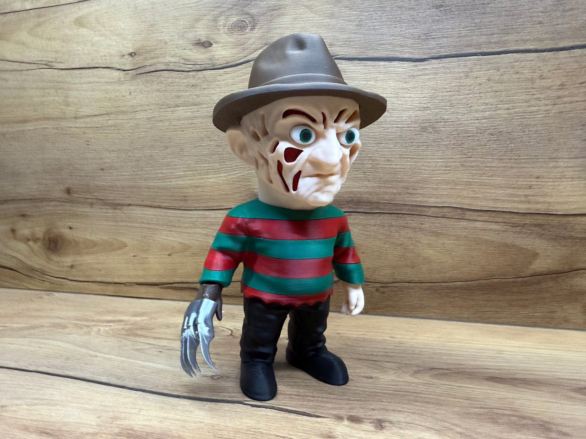 Freddy Krueger Nightmare on Elm Street Minifigure Sculpture — right front three-quarter view showing full face scarred detail from right angle with teal-green eyes, scar tissue masses, open void apertures, felt fedora at three-quarter angle, red and green stripe sweater right arm sleeve detail, four-blade silver razor glove on right hand prominently visible at lower right, bare left hand, black trousers and boots