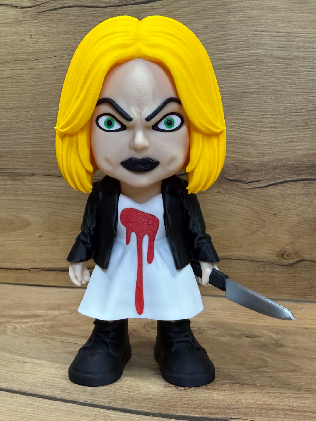 Tiffany Bride of Chucky Minifigure Sculpture — front view showing vivid yellow bob hair, fierce green eyes with black brows and black lips, white dress with sculpted red dripping heart blood stain, open black leather jacket and silver kitchen knife in right hand