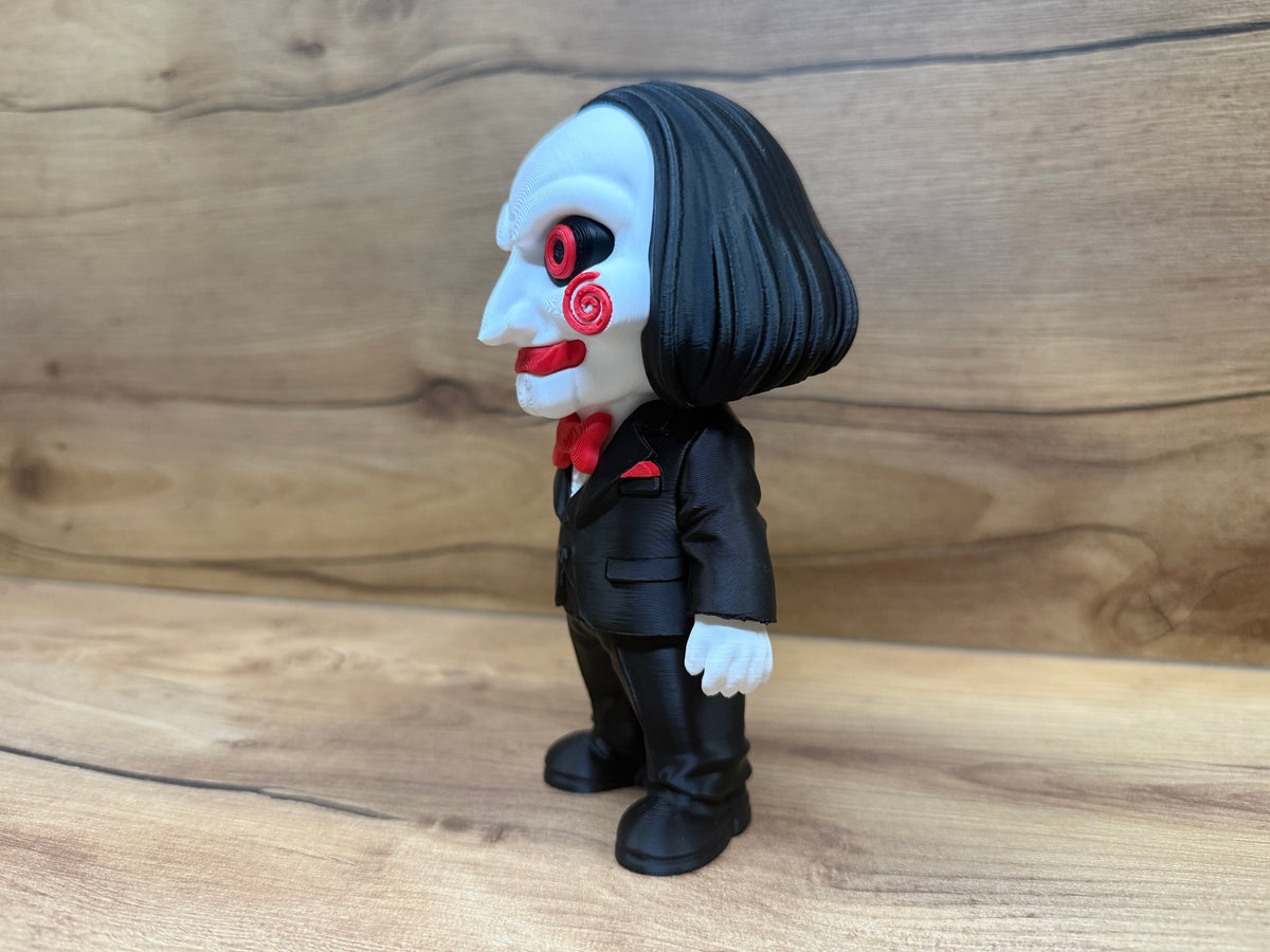 Billy the Puppet Saw Minifigure Sculpture — left front three-quarter view showing left spiral cheek rosette, red eye ring detail, open grin, black hair fall, black suit lapel and red pocket square in breast pocket