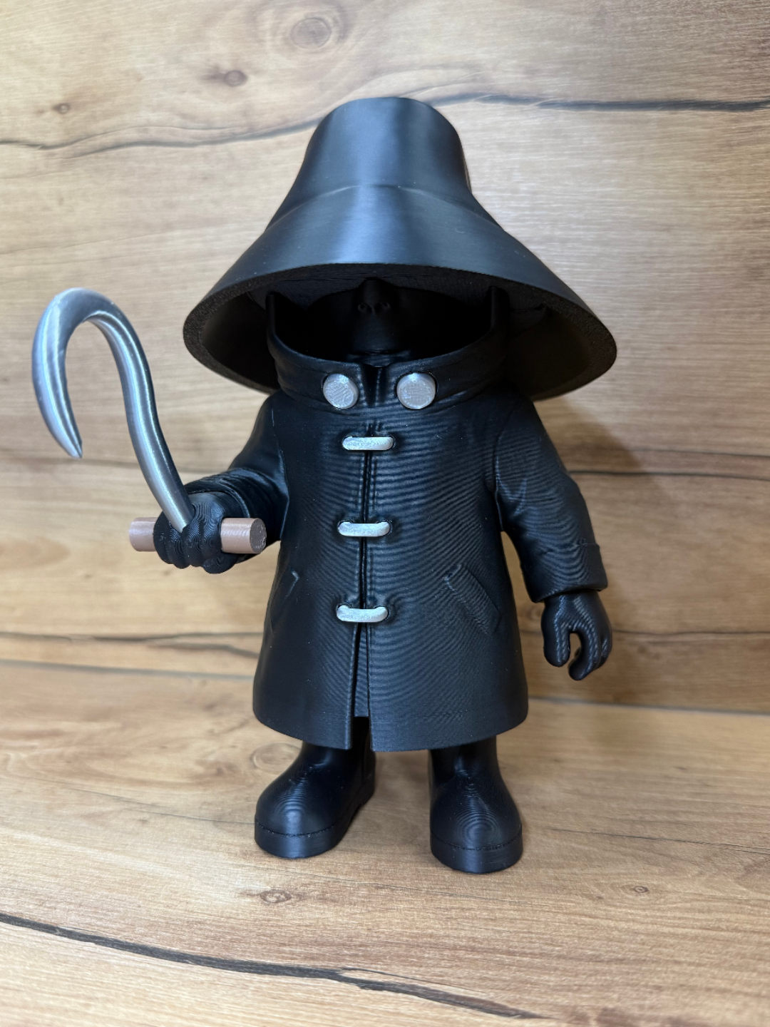 Candyman Horror Minifigure Sculpture — front view showing wide-brimmed black hat casting deep shadow over face with two small silver goggle eye apertures visible, floor-length textured black trench coat with five silver toggle clasp fasteners, right hand raised holding silver hook with wooden handle