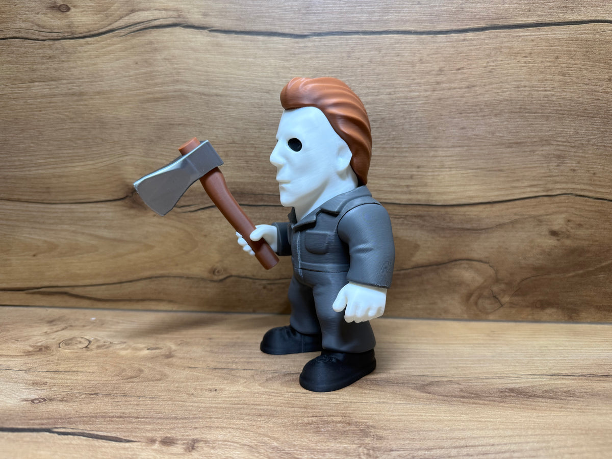 Michael Myers Halloween Minifigure Sculpture — right side profile view showing white mask profile with single black oval eye aperture, auburn hair swept back and flowing behind mask, dark grey coverall right side panel seam lines, right arm extended forward holding silver axe at shoulder height with brown handle, black boot profile and slight forward lean stance