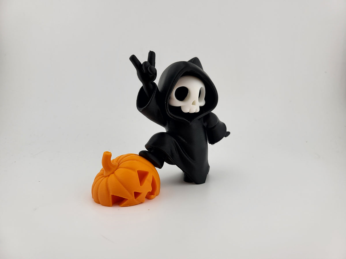 Halloween Reaper Cat Skull Minifigure — right front three-quarter view: matte black robe and cat ear hood from right angle, white skull face with curved smile visible, devil horn gesture overhead, natural sideways leaning pose, vivid orange jack-o'-lantern carved pumpkin at figure left side