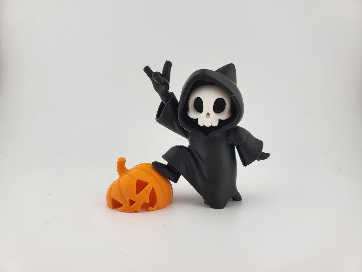 Halloween Reaper Cat Skull Minifigure — front three-quarter view: matte black hooded robe with two cat ear points at hood crown, white rounded skull face with two oval void eyes and curved smile, right hand raised in devil horn gesture, left arm sweeping outward, vivid orange carved jack-o'-lantern pumpkin beside figure