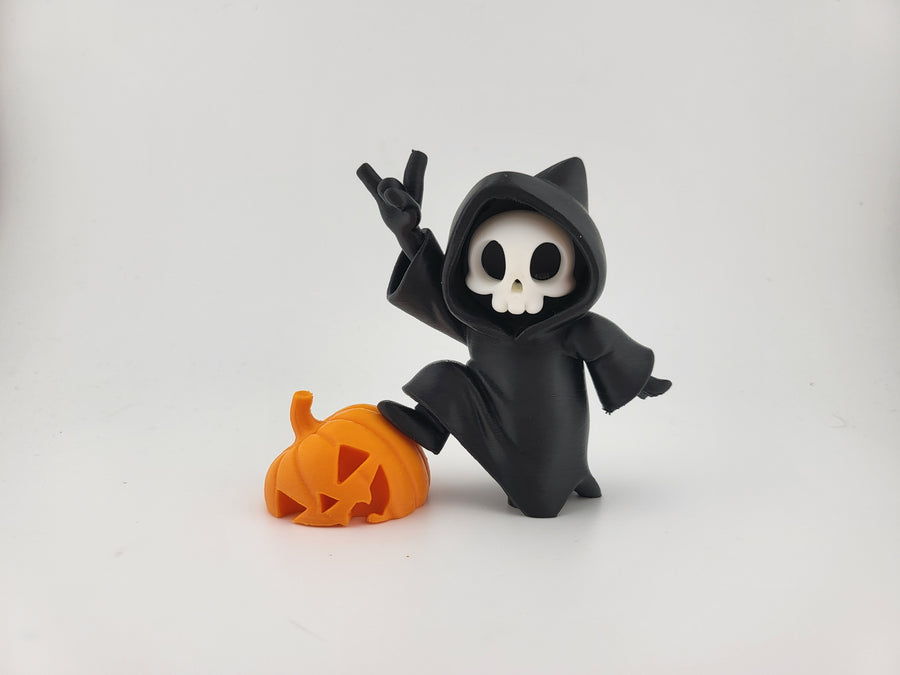 Halloween Reaper Cat Skull Minifigure — front three-quarter view: matte black hooded robe with two cat ear points at hood crown, white rounded skull face with two oval void eyes and curved smile, right hand raised in devil horn gesture, left arm sweeping outward, vivid orange carved jack-o'-lantern pumpkin beside figure