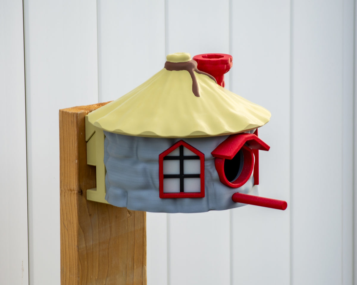 Cottage birdhouse on post showing red entrance frame