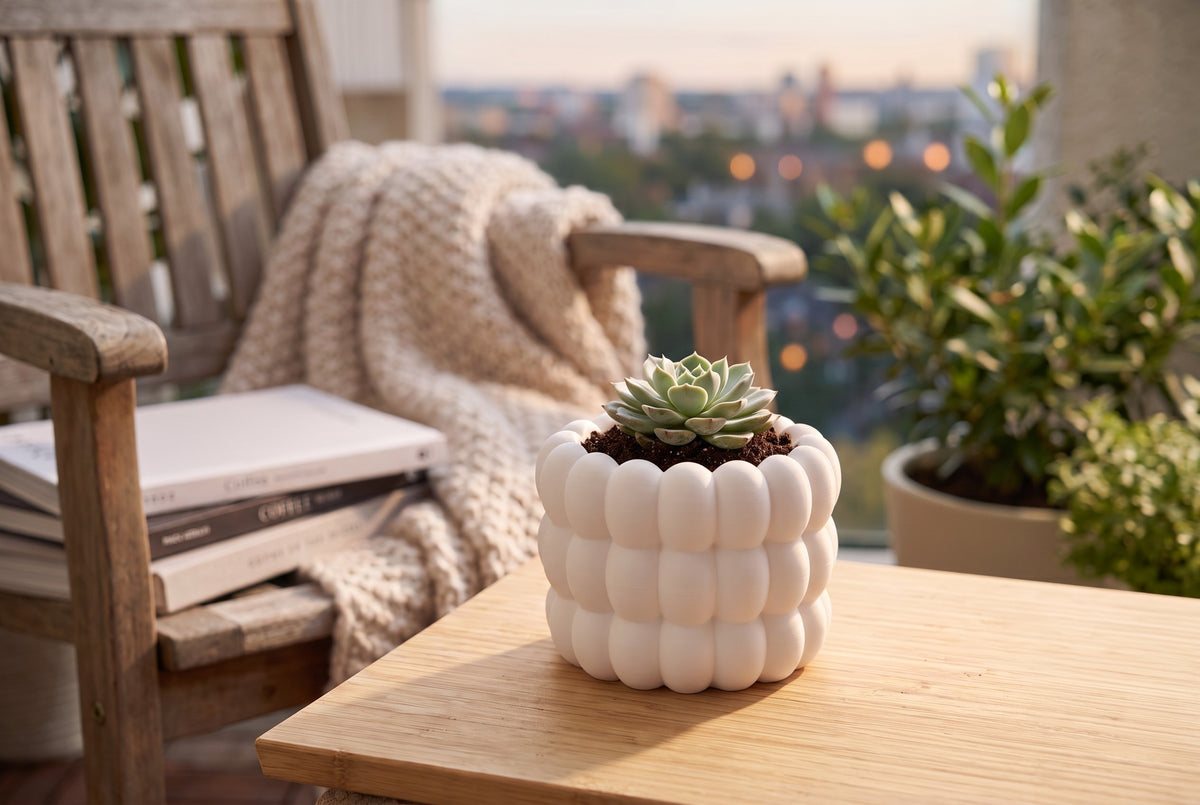 Bubble Plant Pot in white with green succulent on a dark wood sideboard beside a journal, linen throw chair and brass watering can in a warm neutral modern interior with soft window light