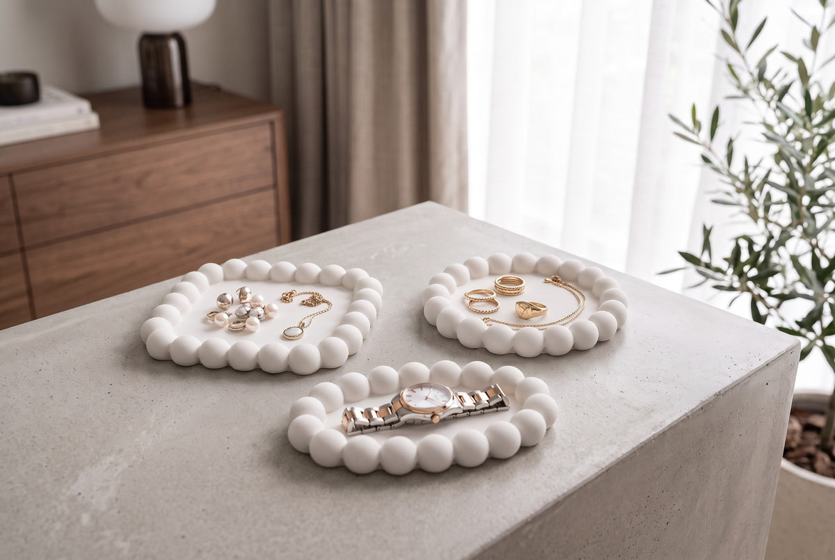 Three white bubble trays with rings, a necklace, earrings and a watch on a beige counter