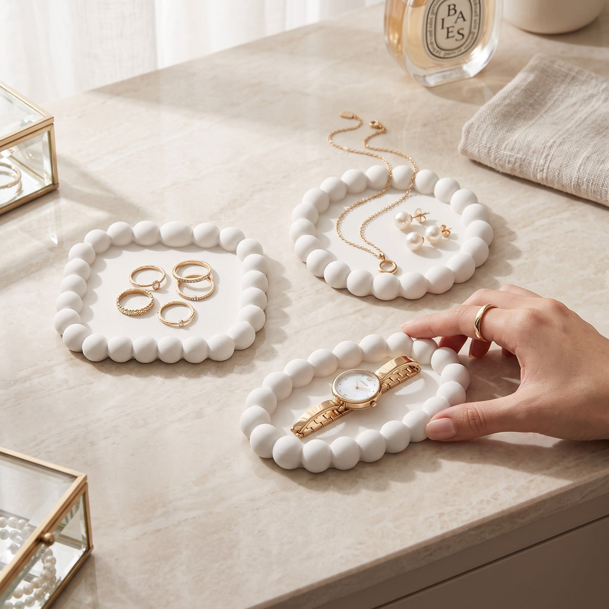 White bubble trays holding rings, a necklace, pendants and a watch on a beige stone table