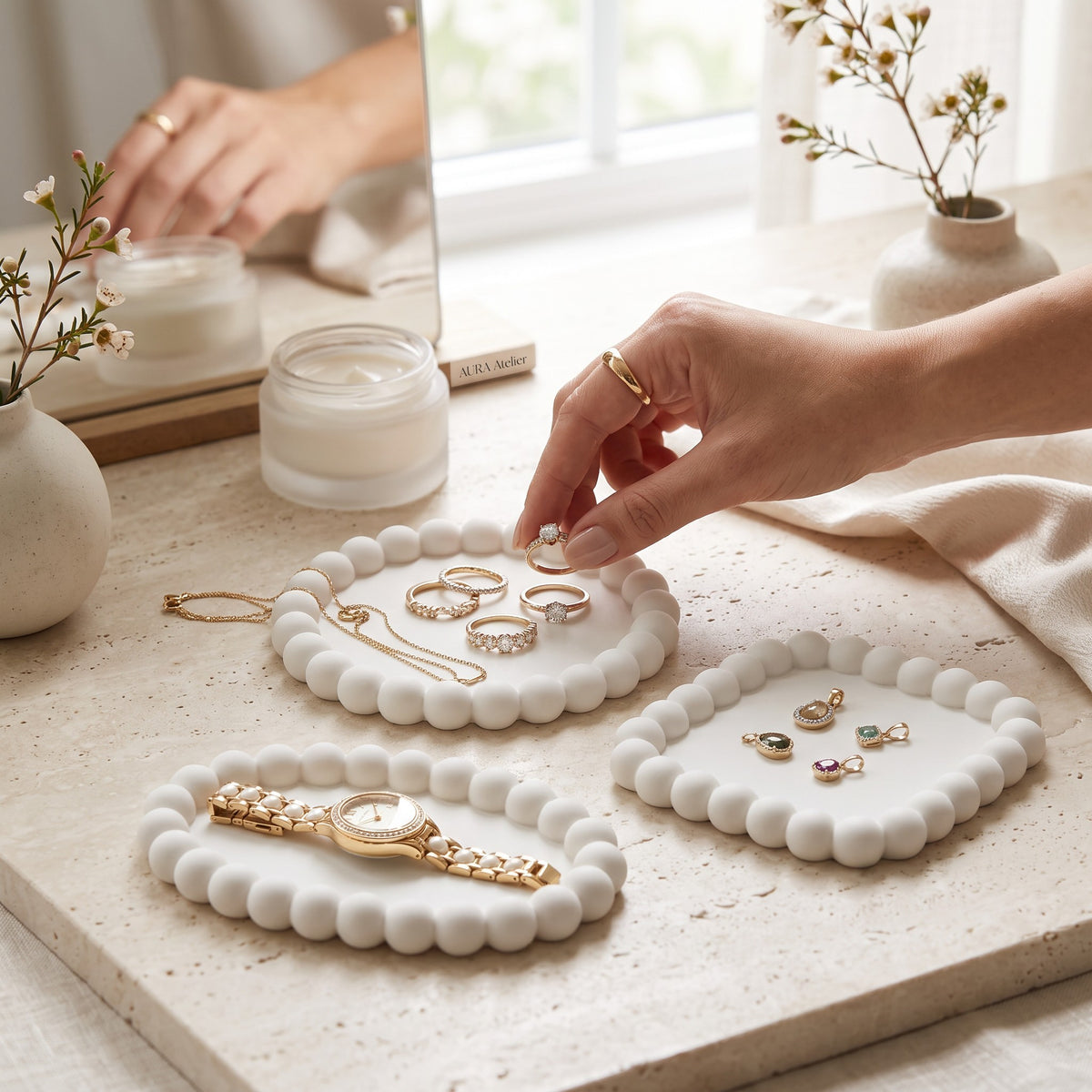 Hands reaching for rings and a watch on white bubble trays on a sunny windowsill