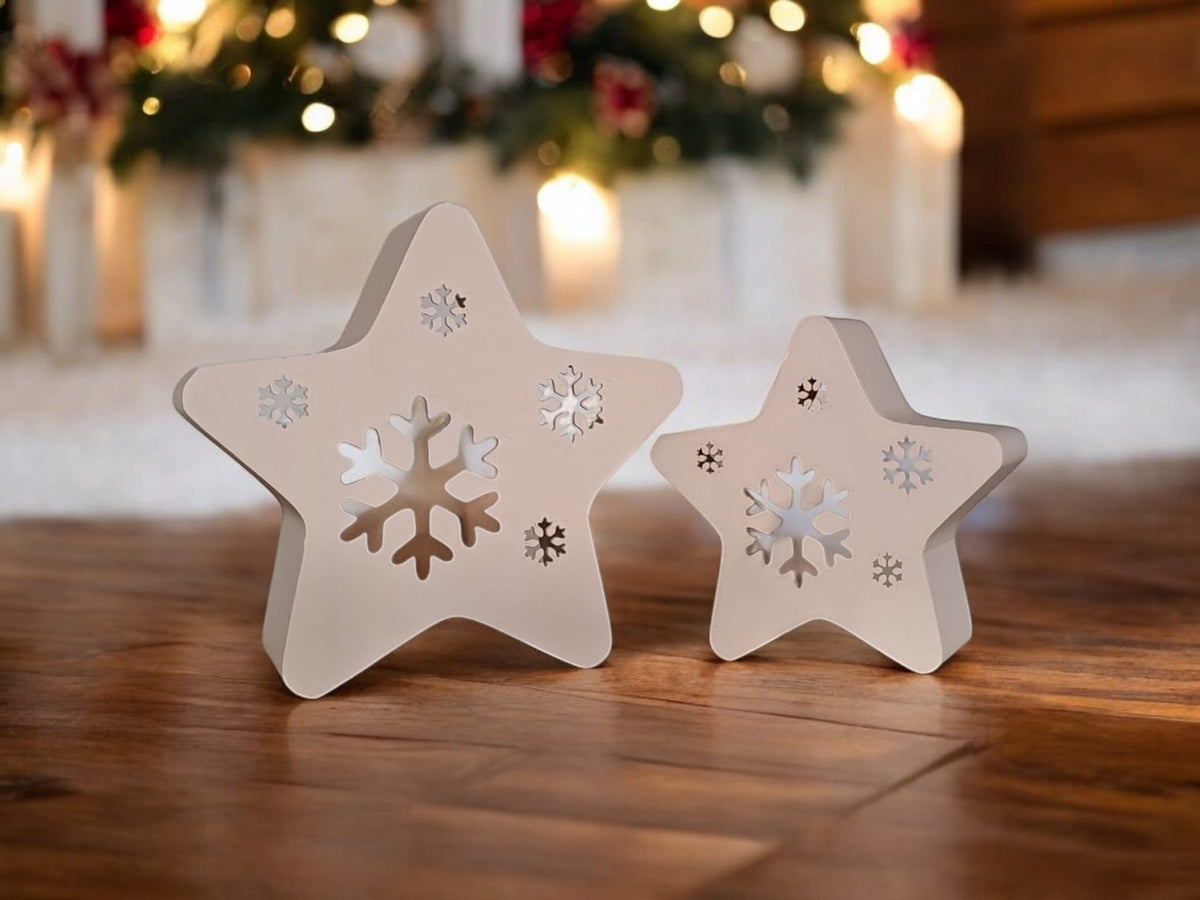 Two white star snowflake tealight holders in snow under frosted Christmas tree fairy lights
