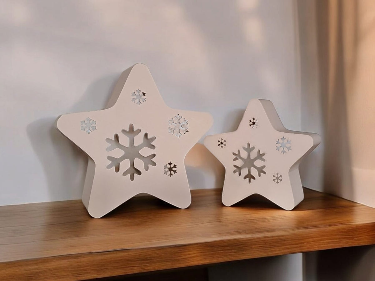Two white star snowflake tealight holders on white fabric surface neutral background