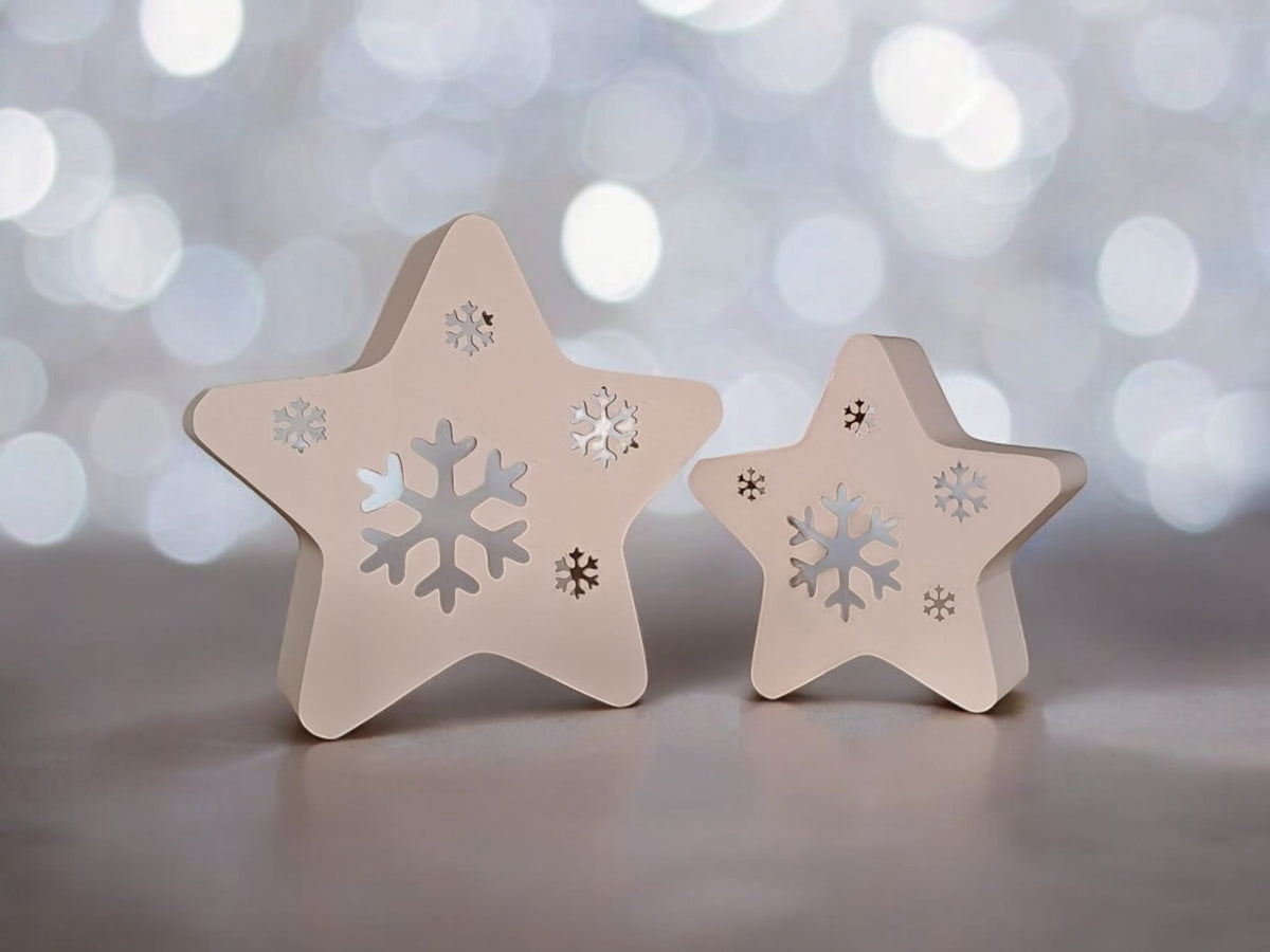 Two white star snowflake tealight holders on rustic wooden table with candle and Christmas tree