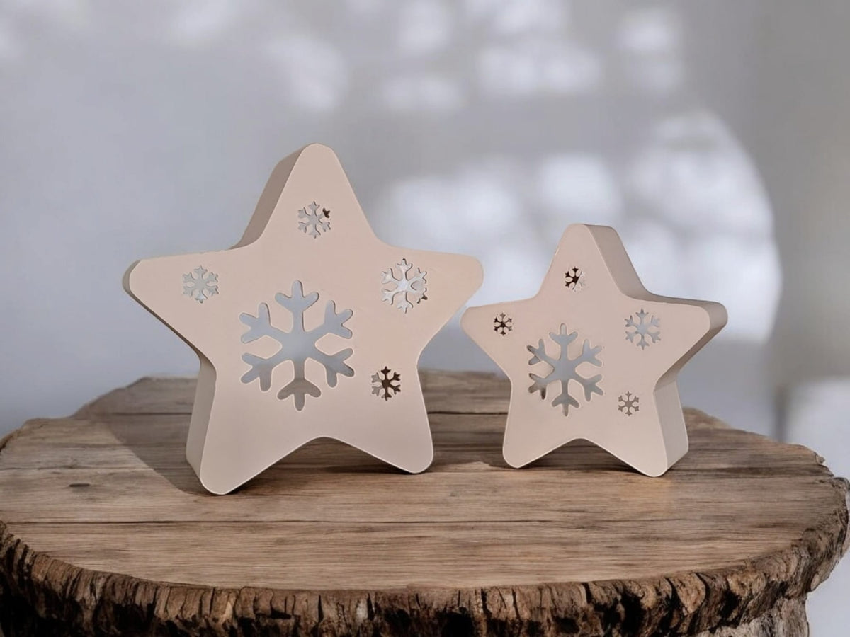 Two white star snowflake tealight holders sitting in snow under Christmas tree branches