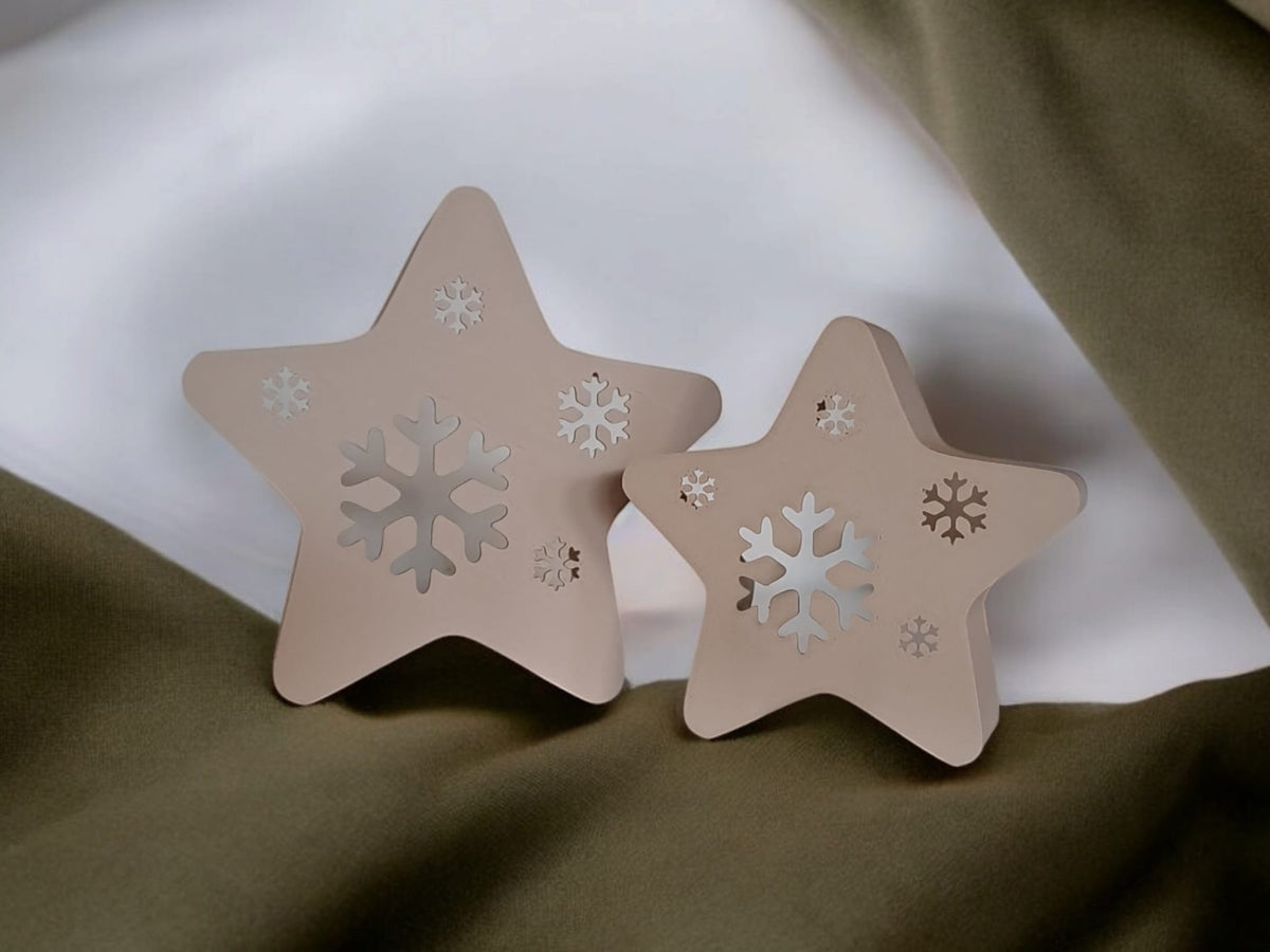 Two star snowflake tealight holders glowing warm amber Christmas tree bokeh background
