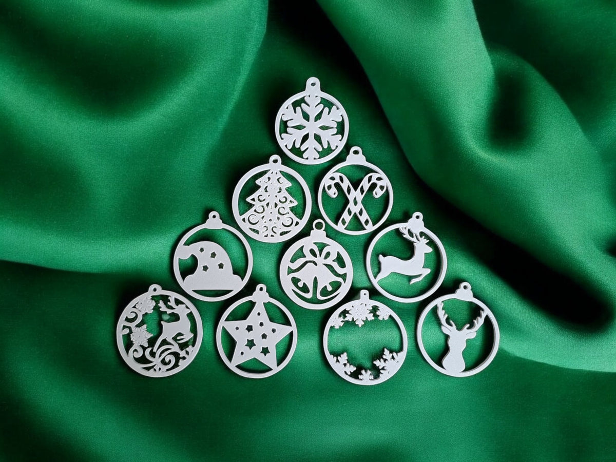Two white plastic filigree Christmas bauble ornament hangers hanging from silver hooks on snow-dusted Christmas pine tree branch warm bokeh golden fairy lights Christmas tree and snowflake designs outdoor festive scene