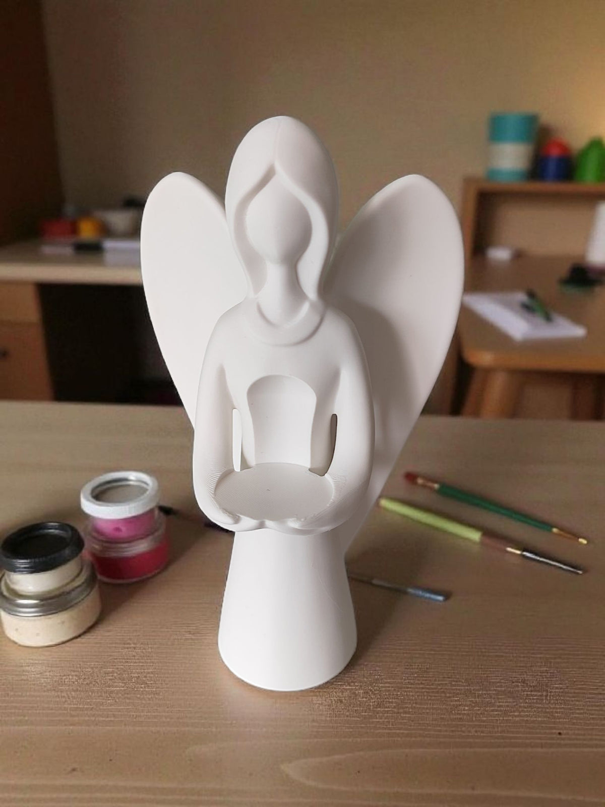 White Christmas angel with tealight on wooden table beside paintbrushes and plant