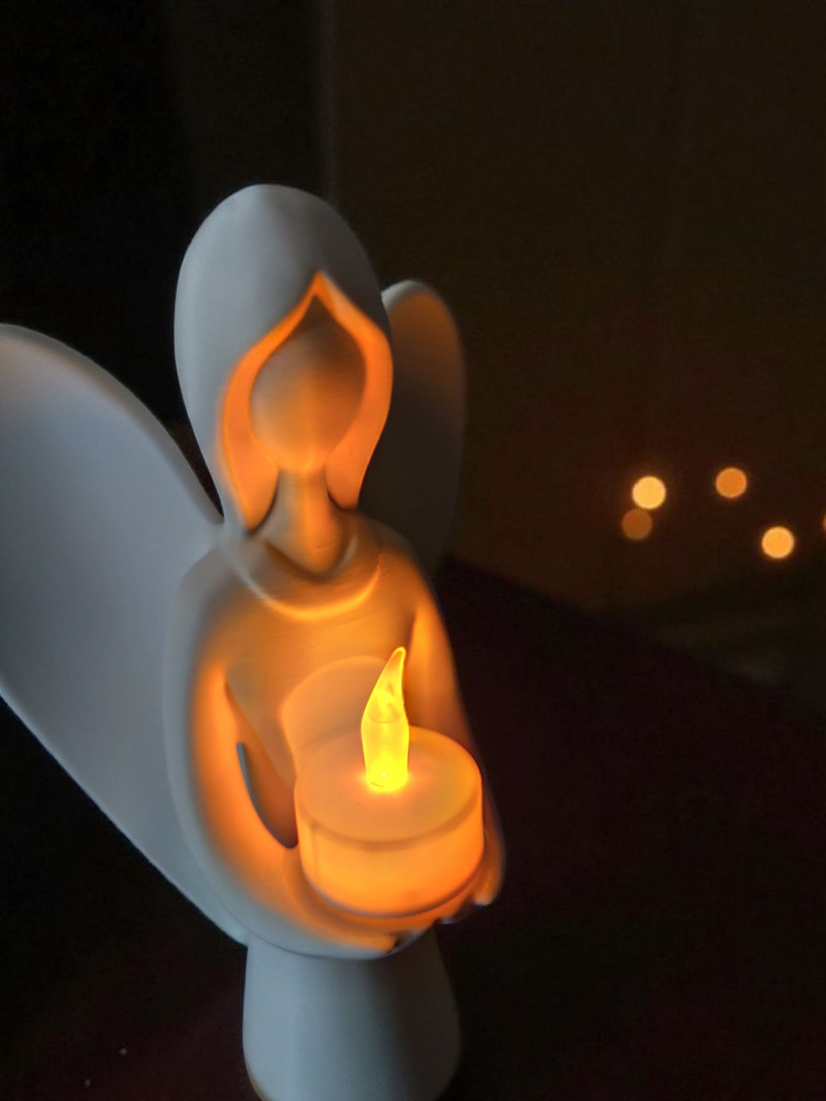 White Christmas angel sculpture holding LED tealight on wooden table with holly and fairy lights