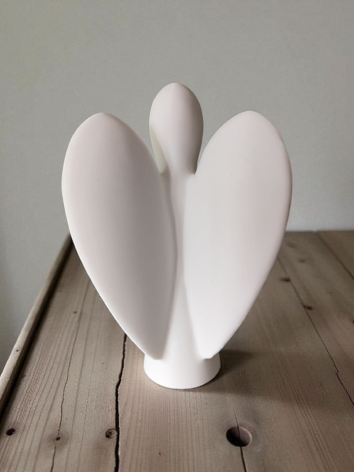 Side view of white angel sculpture on wooden surface matte finish detail