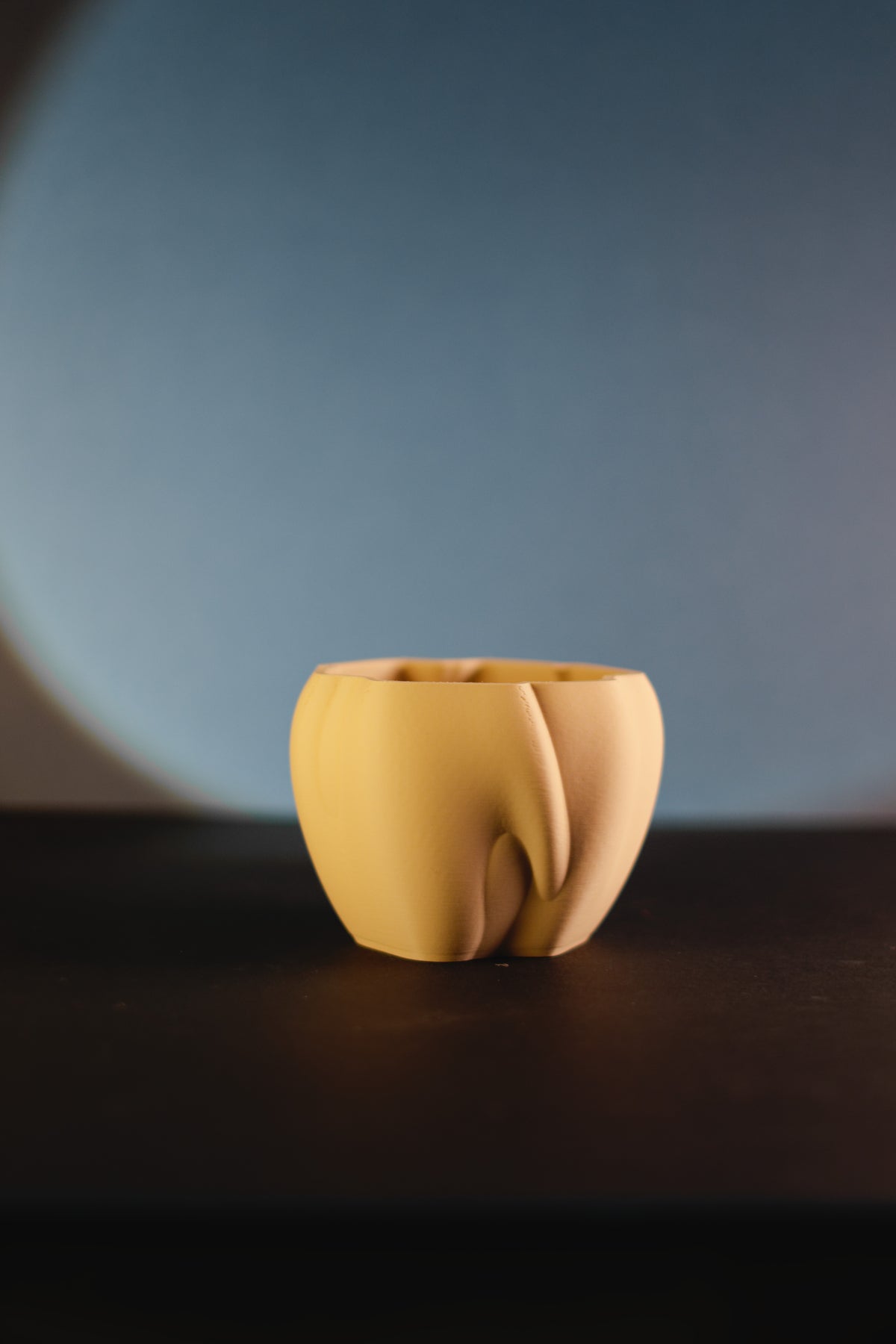 Elegant organic flowing planter yellow matte front view on dark surface moody studio shot
