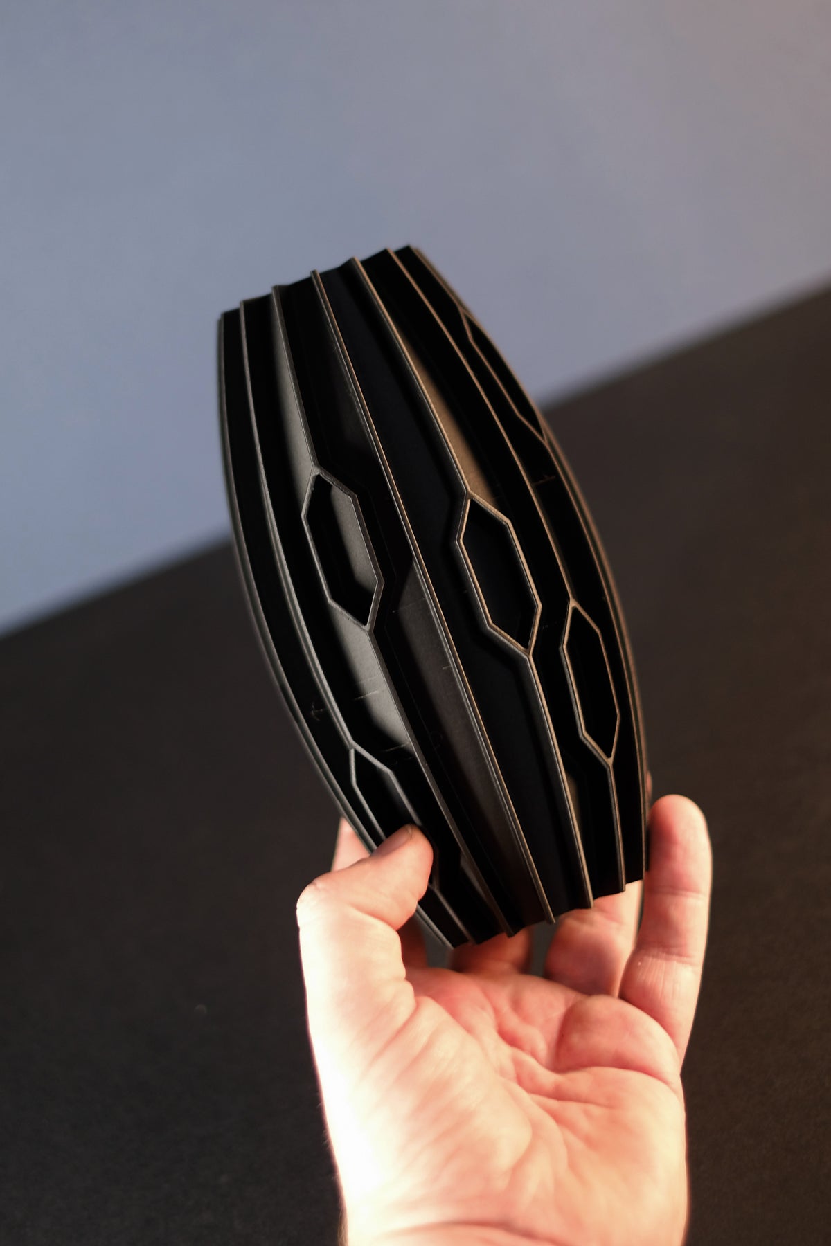 Black diamond rib vase held in two hands showing oval form and staggered geometric pattern lifestyle