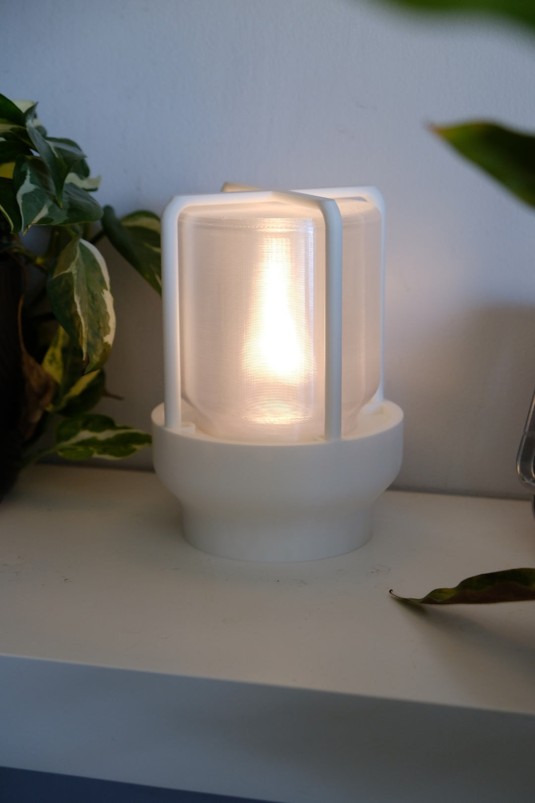 The Miner's Lantern Lamp real photo white on shelf beside black ribbed planter and clock warm amber glow interior lifestyle